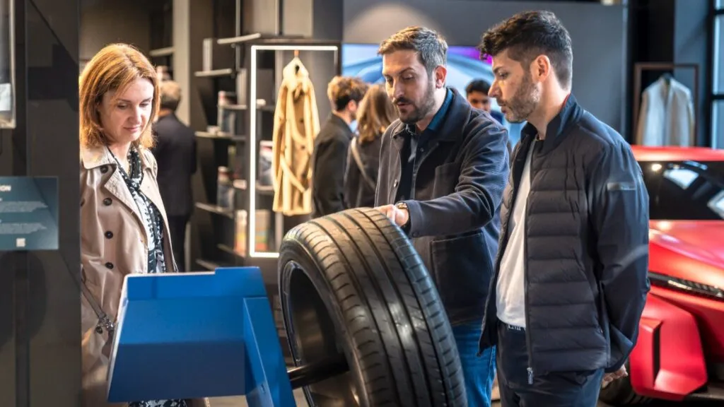 A close-up of the Vredestein Quatrac Pro 2 all-season tyre on display at an exhibition, with attendees discussing the "Passage" themed seasonal graphical elements designed by Italdesign. Photo Credit: Apollo Tyres