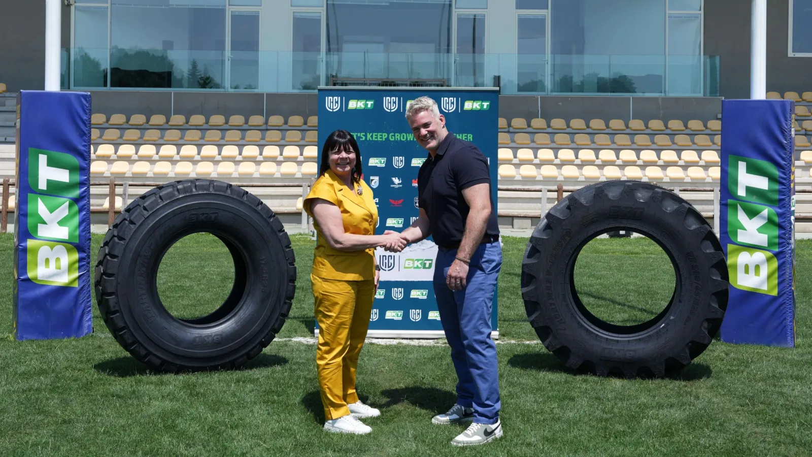 Lucia Salmaso and Martin Anayi shaking hands on a rugby field between two large off-highway tyres and BKT branding posts. (Photo: BKT)