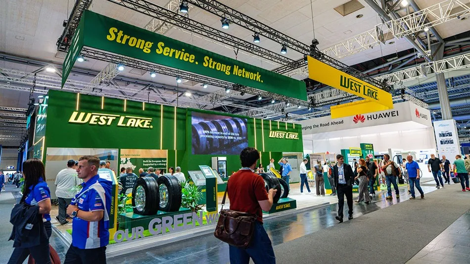 Crowded exhibition booth at IAA Transportation with prominent green and yellow Westlake branding hanging banners, displays of commercial truck tyres, and visitors walking through.