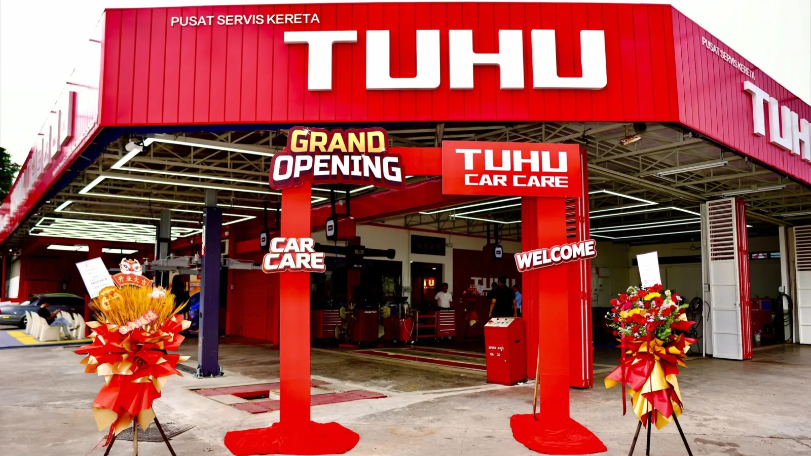 Front view of a red Tuhu Car Care service center with grand opening floral stands and a red entrance archway in front of workshop bays.