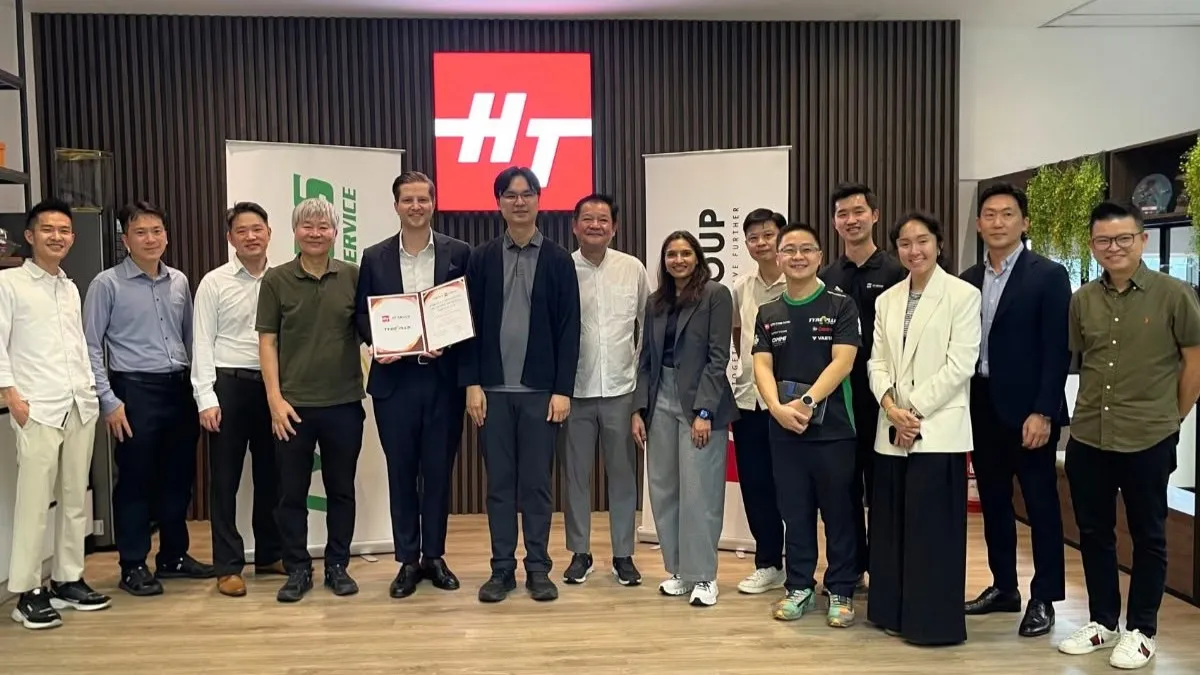 Group of executives and team members from Michelin and HT Group standing together in front of a red HT Group logo backdrop, with leaders holding a signed certificate.
