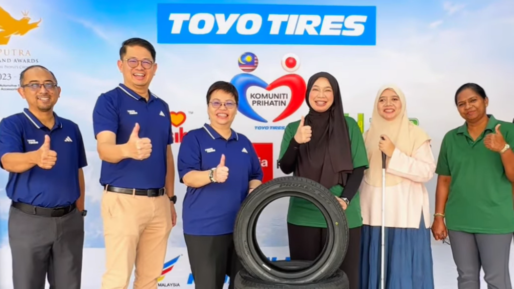 Representatives from Toyo Tyre Malaysia and MAB standing together smiling with thumbs-up gestures behind stacked Toyo Proxes CR1 tyres in front of a Komuniti Prihatin Toyo backdrop.