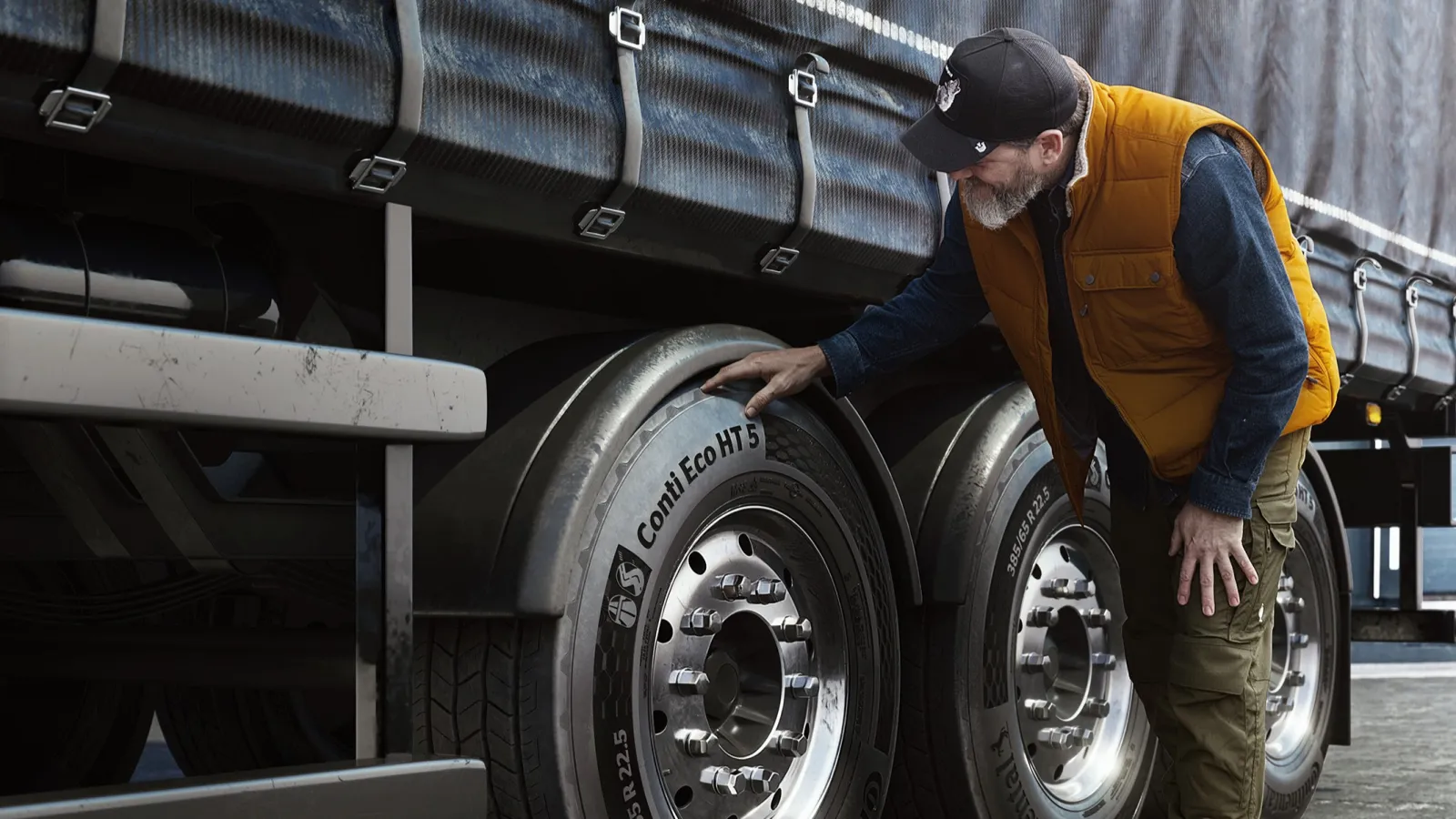 A man wearing an orange vest and black cap leaning down to inspect a Continental Conti Eco HT 5 trailer tyre fitted on a commercial semi-trailer wheel axle.